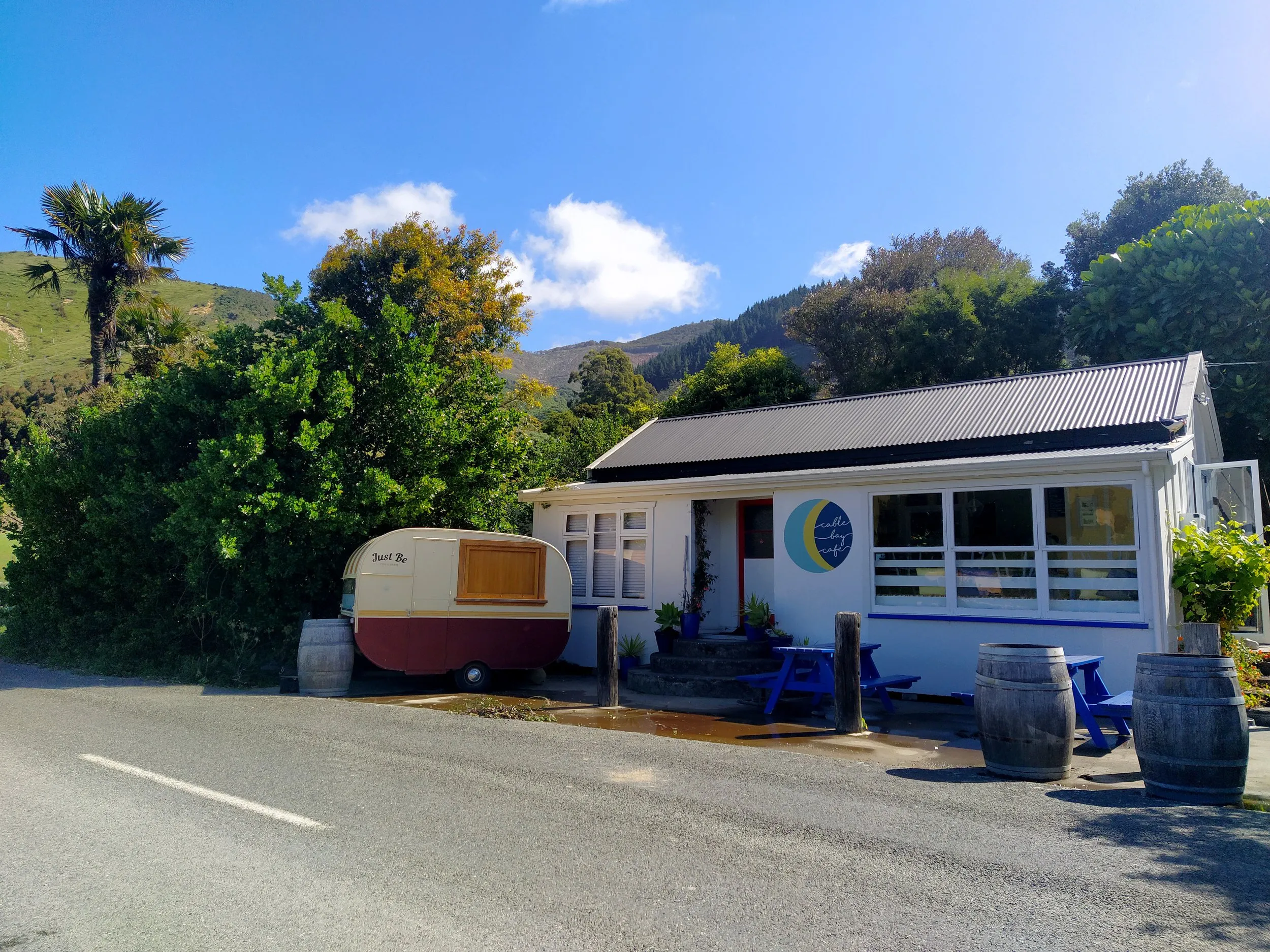 The white weatherboard café with its round logo, a vintage caravan and wine barrels by the road, bush-covered hills behind